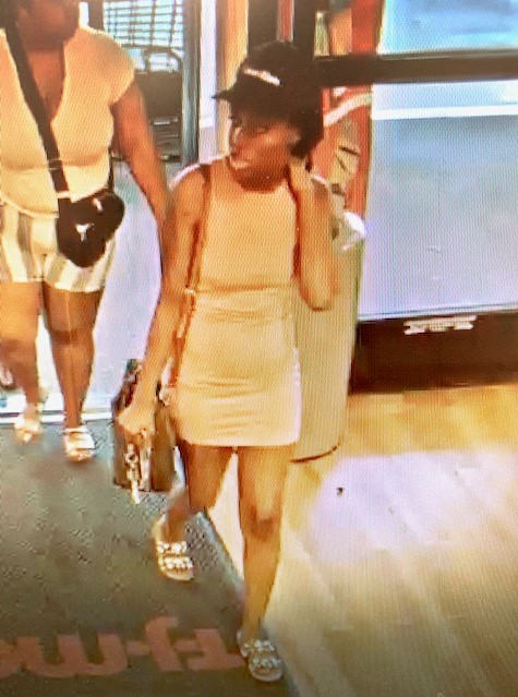 Photo of female in short, gray sleeveless dress with black ball cap and white sandals with a brown cross-body purse. 